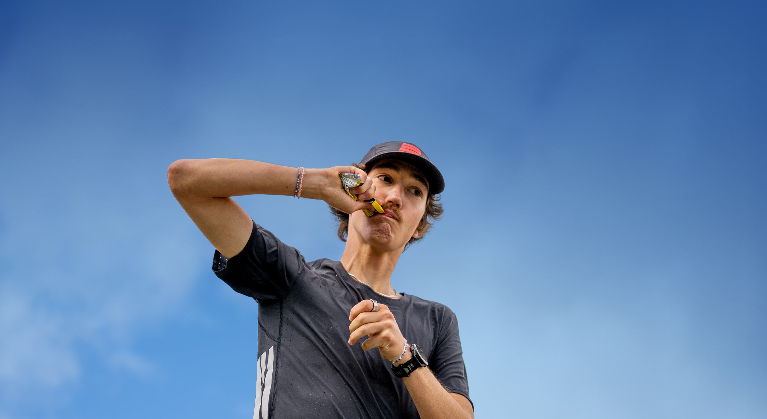 Runner refueling with a Powerbar energy gel outdoors under a blue sky during training.