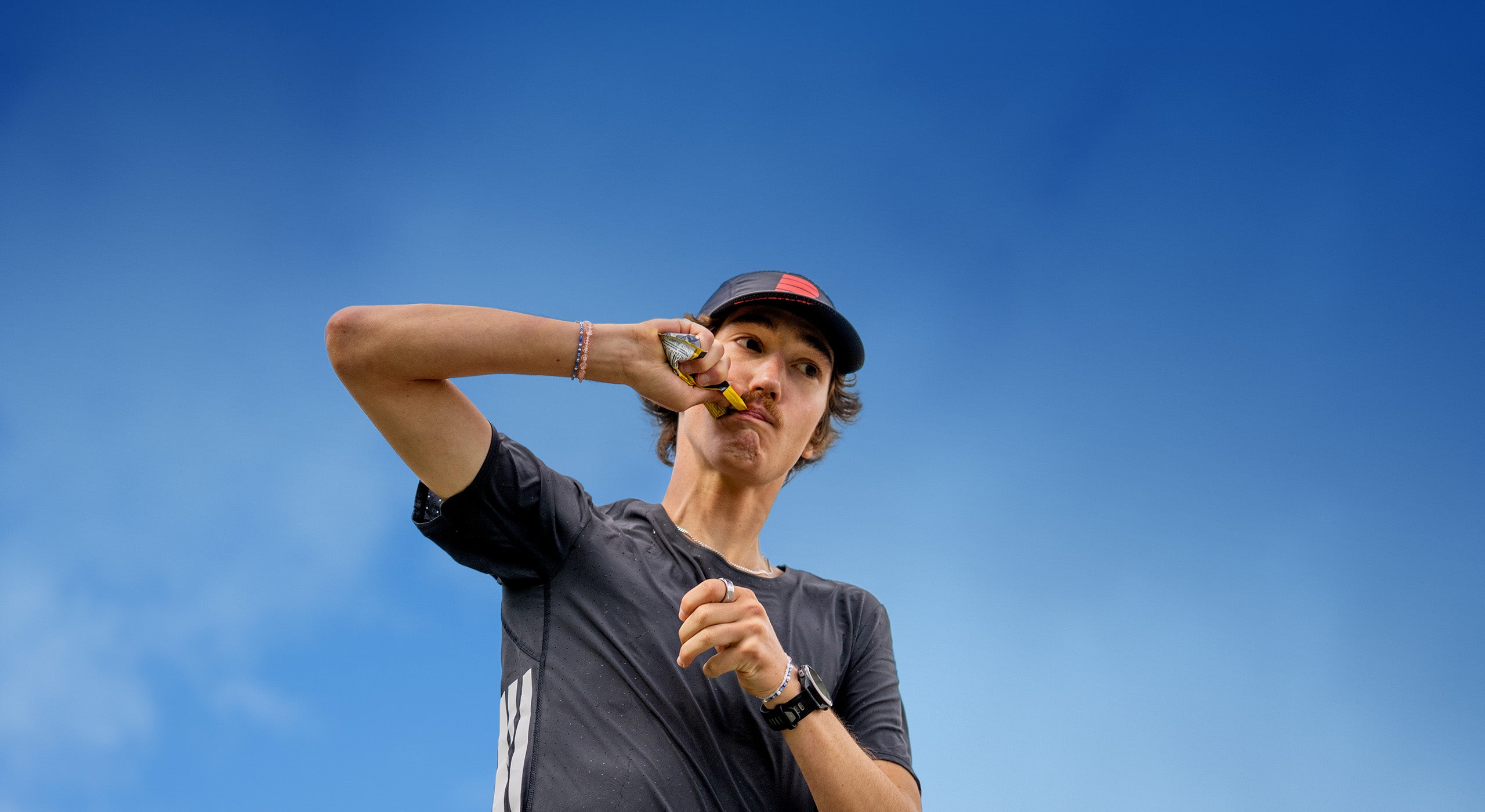 Runner refueling with a Powerbar energy gel outdoors under a blue sky during training.